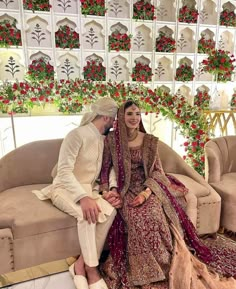 a man and woman sitting on a couch in front of a wall with red flowers