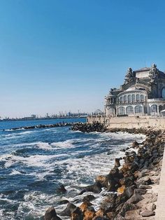 an old building sitting on top of a cliff next to the ocean with waves crashing in front of it