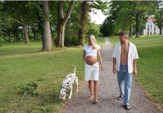 a man and woman walking down a path with a dalmatian dog next to them