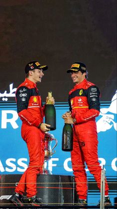 two men standing on top of a race podium holding onto bottles in each hand and looking at each other