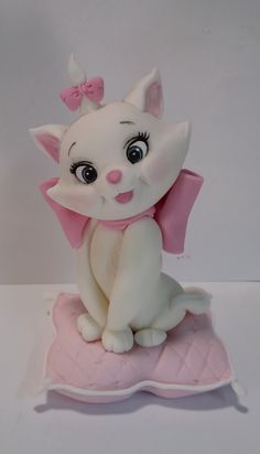 a white cat figurine sitting on top of a pink cushion with a bow