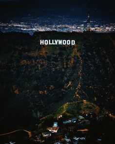 the hollywood sign is lit up at night on top of a mountain with city lights in the background