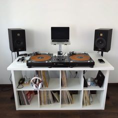 a record player sitting on top of a white shelf next to two speakers and a laptop computer