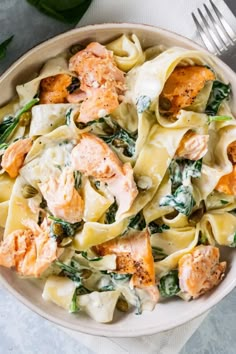 a white bowl filled with pasta and salmon on top of a blue table cloth next to a fork