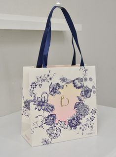 a white bag with purple flowers and a blue ribbon hanging from it's handle