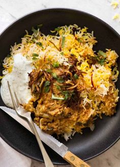 a black plate topped with rice and meat next to a fork on top of a table