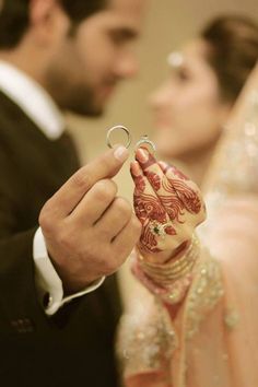 the bride and groom hold their wedding rings in front of them as they look at each other