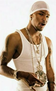 a man wearing a white tank top and gold chains holding a cell phone in his hand