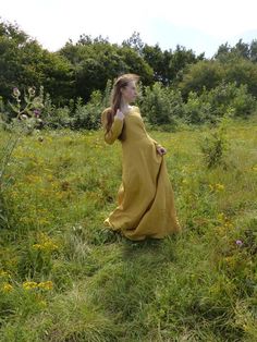 a woman in a yellow dress is walking through the grass with her hands behind her head