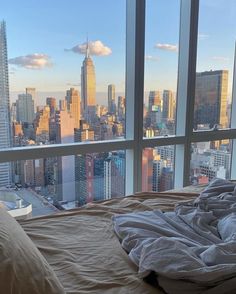 an unmade bed in front of a large window overlooking the cityscape and skyscrapers