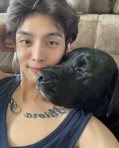 a young man is hugging his dog on the couch with tattoos on his chest and neck