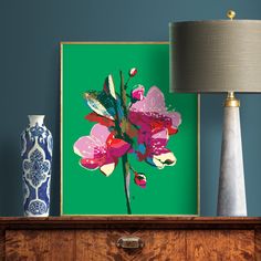 a painting is displayed on a dresser next to a lamp and vase with flowers in it