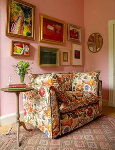 a living room with pink walls and pictures on the wall above the couch is decorated with flowers