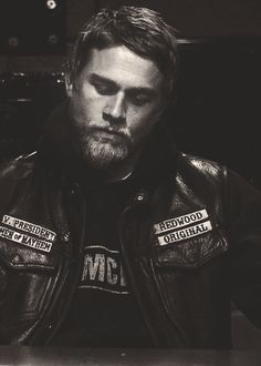 a man in leather jacket sitting at a table with his hands on his hips and looking off to the side