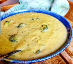 a blue bowl filled with broccoli soup on top of a wooden table