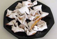 some food that is sitting on a black plate with powdered sugar and orange peels