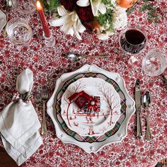 the table is set for christmas dinner with red and white flowers, silverware, napkins, and candles