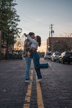 a man and woman kissing on the street in front of some parked cars at sunset