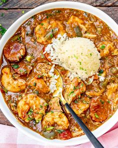 a white bowl filled with shrimp and rice on top of a wooden table next to a spoon