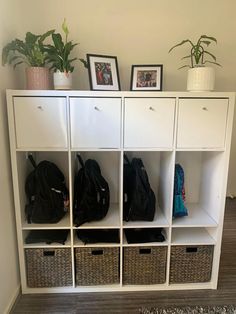 a white shelf filled with lots of bags and baskets next to a wall mounted plant