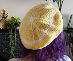 a woman with purple hair wearing a knitted yellow and white ball cap on her head