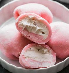 three pink donuts in a white bowl on a black surface with one half eaten