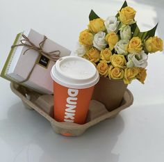 a coffee cup and some yellow roses in a paper container with a bow on it