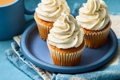 three cupcakes with white frosting on a blue plate next to a coffee mug