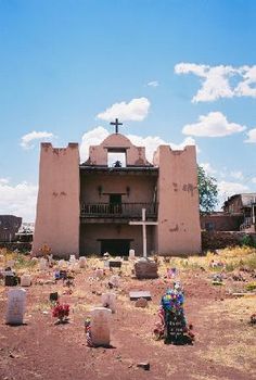 an old church with tombstones in front of it and a cross on the ground