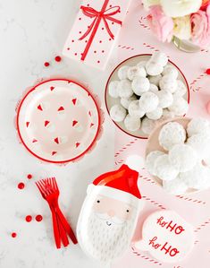 a table topped with plates and bowls filled with marshmallows next to a santa clause