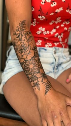 a woman's arm with flowers and leaves on it, sitting in front of a table