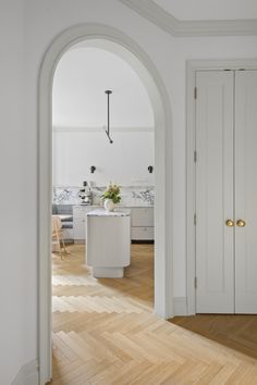 an archway leading into a kitchen with white cabinets and wood flooring on either side