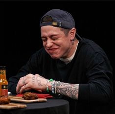 a man sitting at a table with food in front of him and bottles behind him