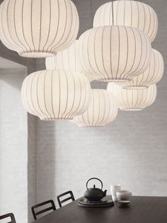 several white lanterns hanging from the ceiling above a table with black chairs and cups on it