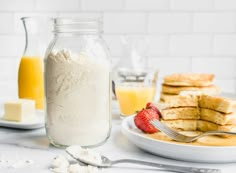 a plate with pancakes, butter and strawberries next to a glass of orange juice