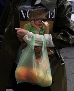 a woman holding a plastic bag full of oranges and an apple in her hand