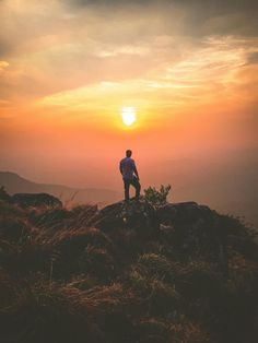 a man standing on top of a lush green hillside under a cloudy sky at sunset