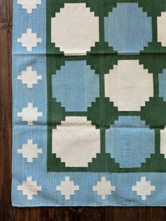 a blue and green quilt with white crosses on it's sides, sitting on a wooden floor