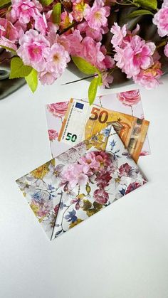 some pink flowers are next to an envelope with 50 euros bill sticking out of it