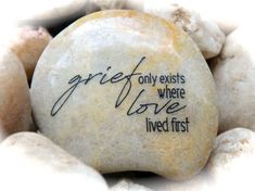 a rock with writing on it surrounded by white rocks and stones that read, griefy exists where love lived first