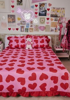 a pink bed with red hearts on it and a teddy bear sitting on the pillow