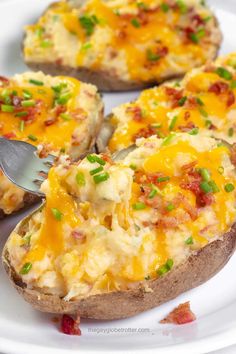 baked potatoes topped with cheese and green onions on a white plate next to a fork