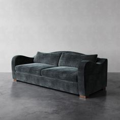 a gray couch sitting on top of a floor next to a white wall and wooden legs