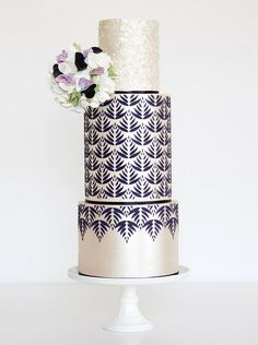 a three tiered wedding cake with purple and white flowers on the top, sitting on a pedestal