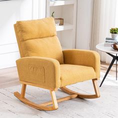 a yellow rocking chair sitting on top of a white rug next to a table with a potted plant