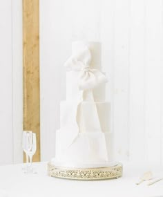 a white wedding cake sitting on top of a table next to wine glasses and utensils