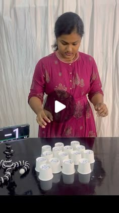 a woman standing in front of a table with cups on it and an object behind her