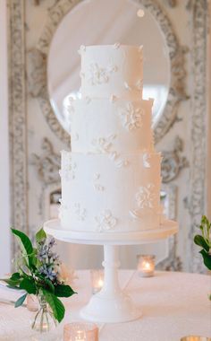 a white wedding cake sitting on top of a table next to candles and greenery