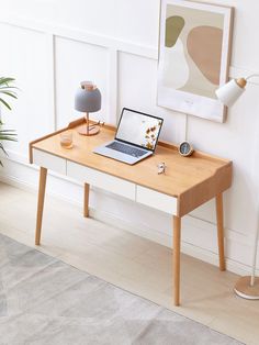 a laptop computer sitting on top of a wooden desk next to a lamp and potted plant