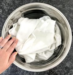 a woman's hand on top of a white cloth in a metal bowl